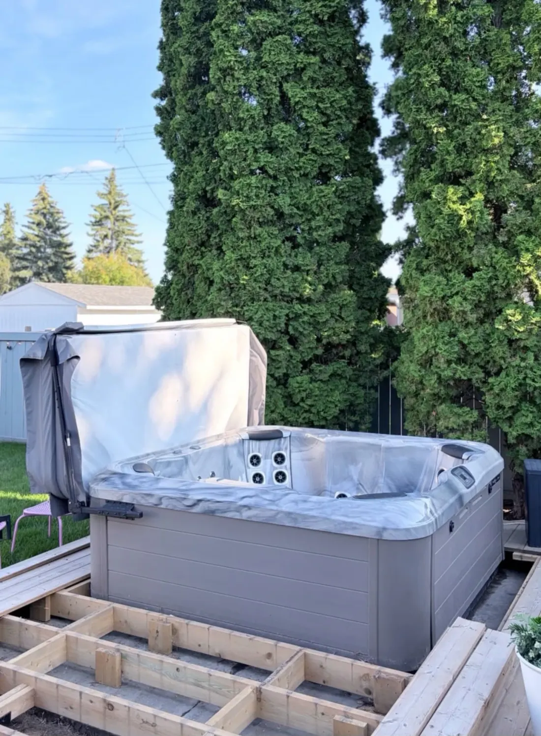 Hot tub with its cover lifted beside a new deck frame in a backyard, set in place by EC Movers