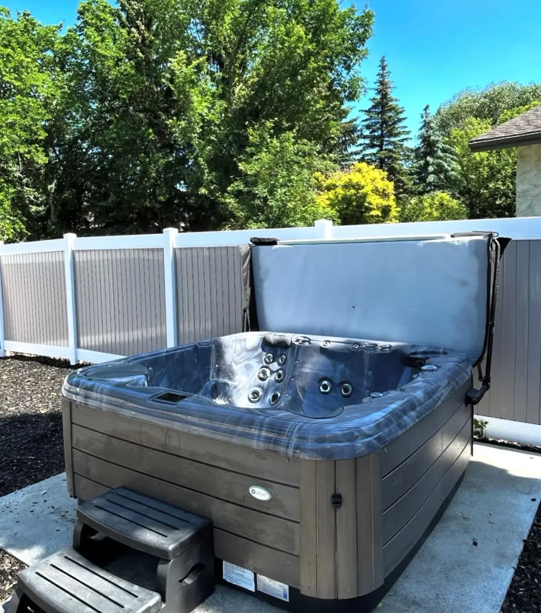 Hot tub with its cover lifted, set on a concrete pad beside a fence after an EC Movers move