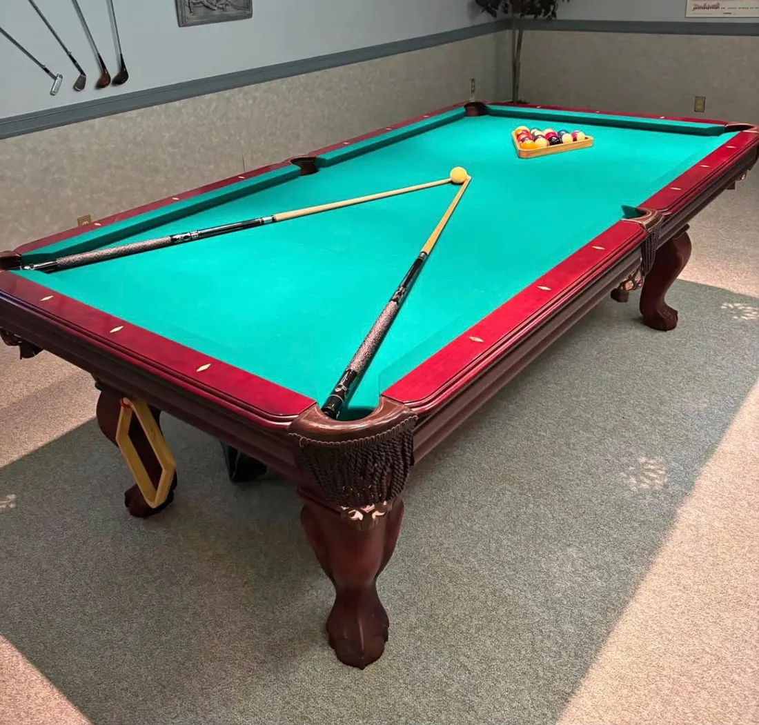 Finished pool table with green cloth, cues and balls racked in a game room
