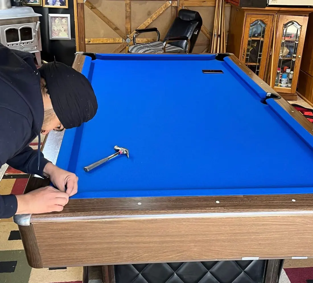 New blue felt being fitted on a pool table by the EC Movers crew